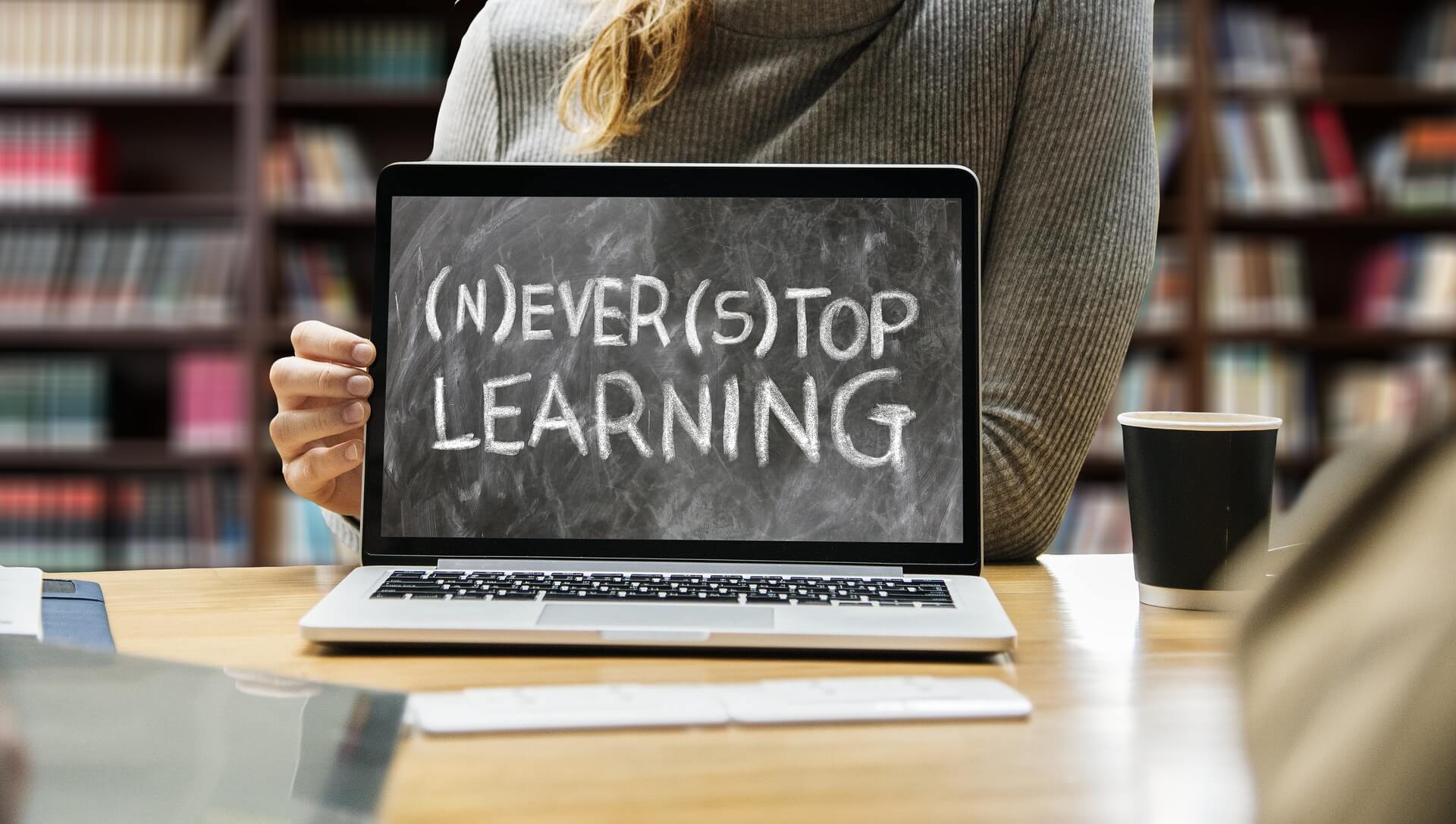 A woman is showing her laptop screen with a message saying "Never Stop Learning".
