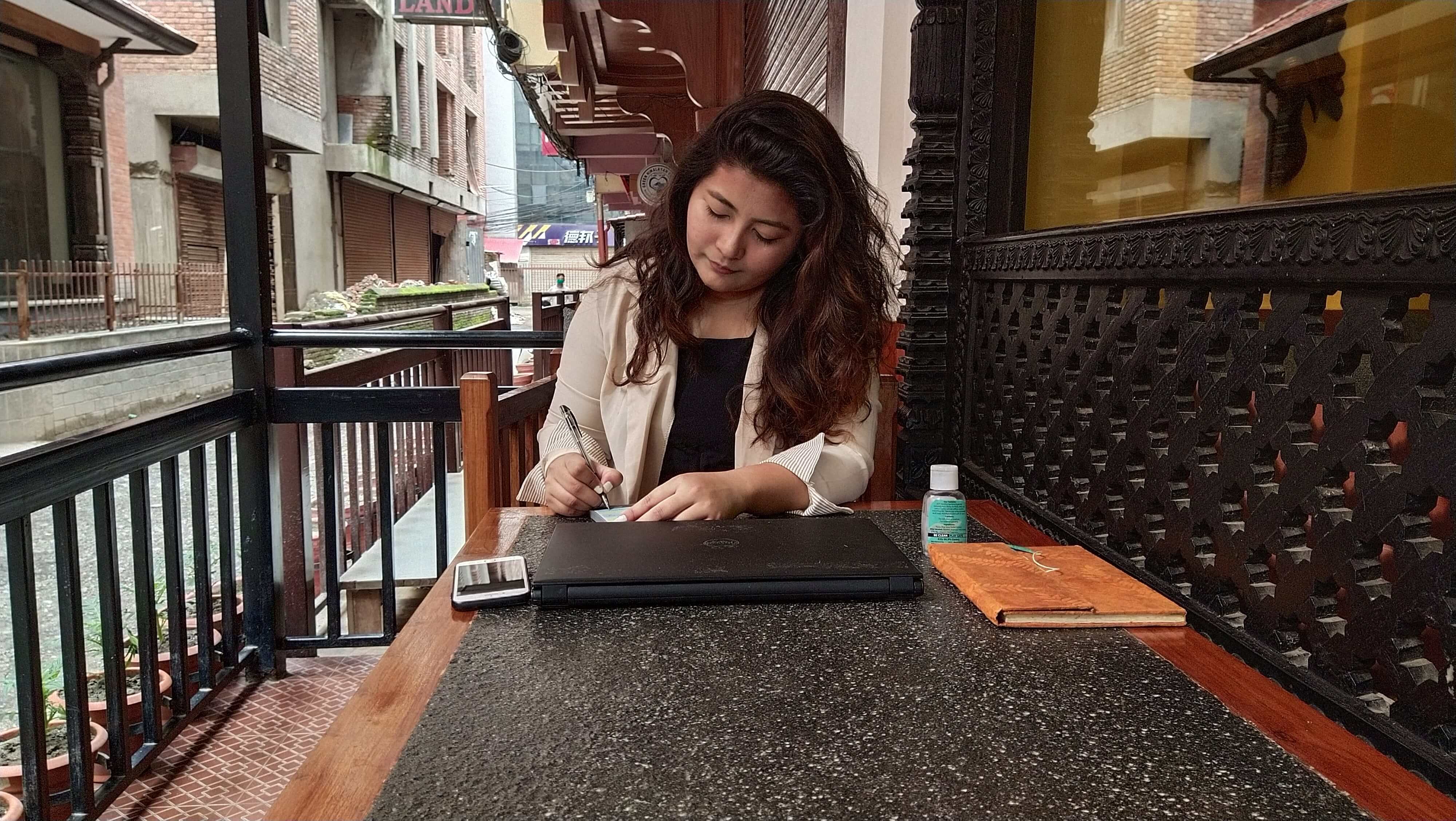 A female student taking some notes along with her laptop and mobile device.